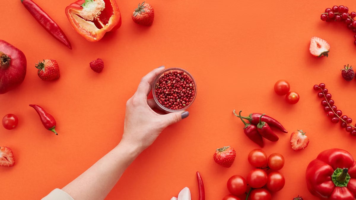 A vibrant display of red fruits and vegetables on a red background with space for text.